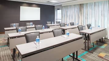 Un salón de conferencias con varias mesas, sillas y botellas de agua.