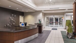 A hotel reception area with a wooden reception desk, a digital screen, and a glass door entrance. - Residence Inn by Marriott Harrisonburg (Harrisonburg)