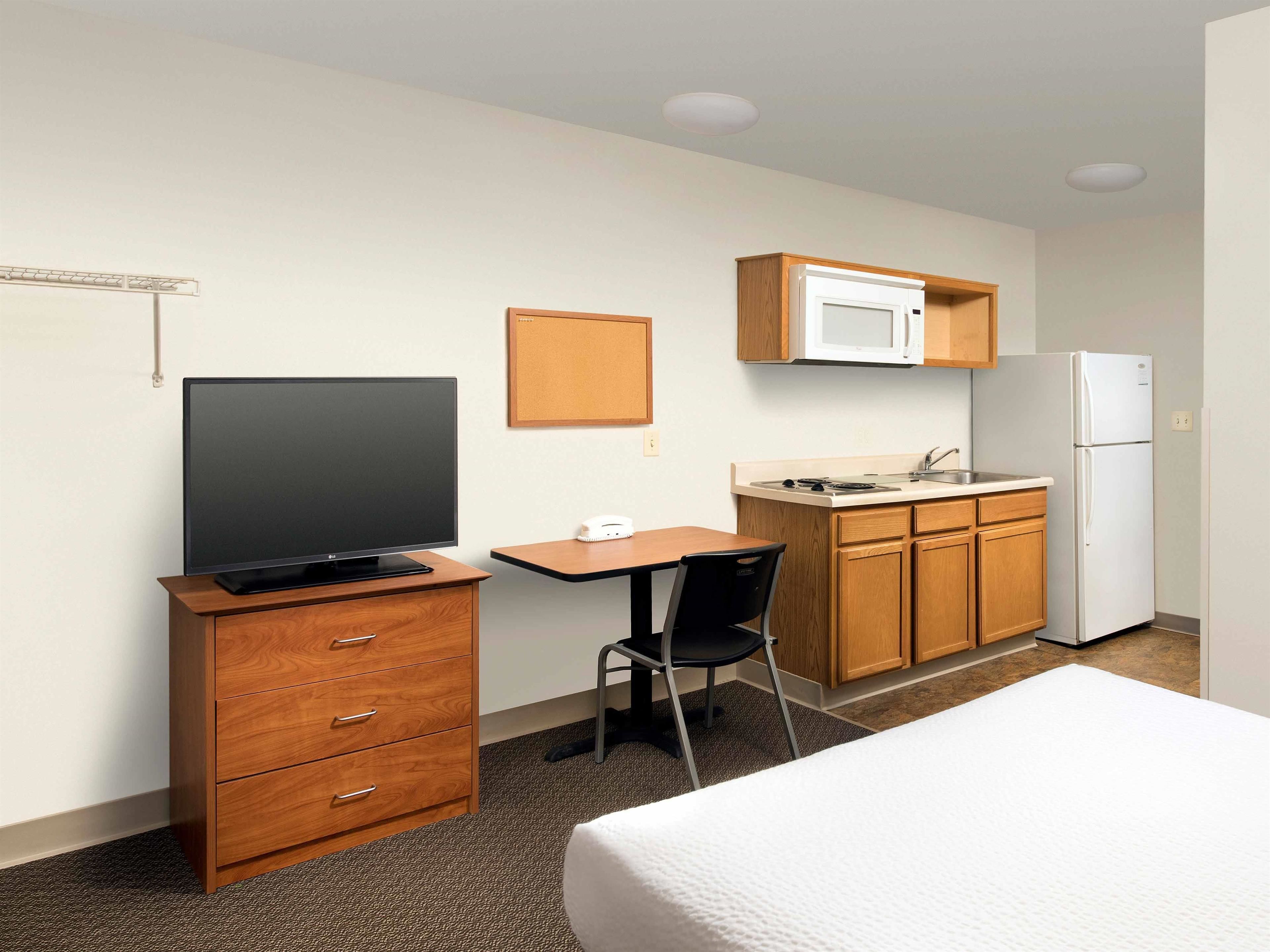 Ein Hotelzimmer mit Bett, Schreibtisch mit Stuhl, Fernseher, Mikrowelle, Kühlschrank und einer kleinen Küchenzeile.