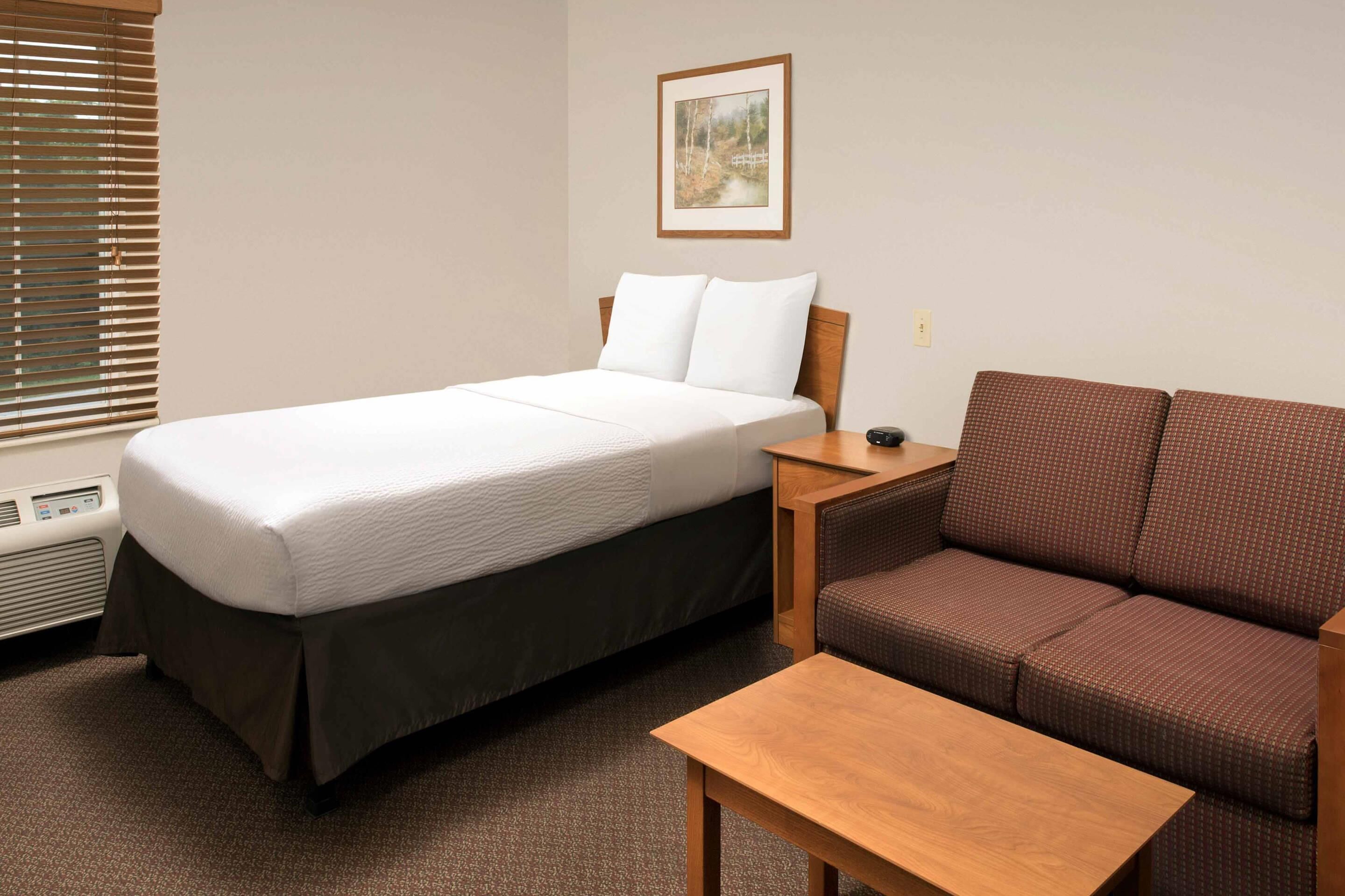 Una habitación de hotel con una cama, un sofá marrón, una mesa de madera y un cuadro en la pared.