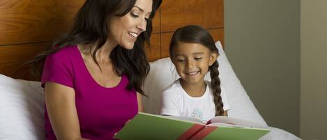 A woman and a child reading a book together on a bed with a wooden headboard.