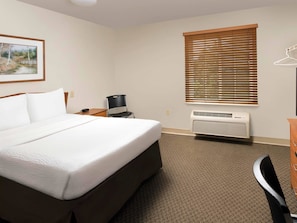 Ein Hotelzimmer mit Bett, Sessel, Schreibtisch, Heizkörper und einem Fenster mit Jalousien.