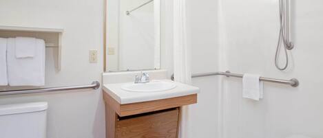 A modern bathroom with a white sink, wooden vanity, a mirror, a shower with a handheld showerhead, and a grab bar.