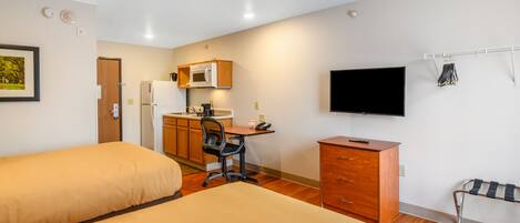 A hotel room with two beds, a kitchenette, a desk, a TV, and a coat rack.