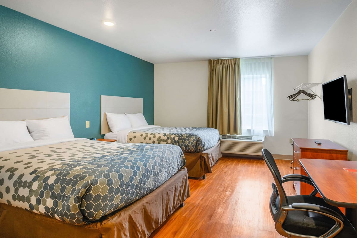 A hotel room with two beds, a desk, a chair, a TV, and a window with curtains.