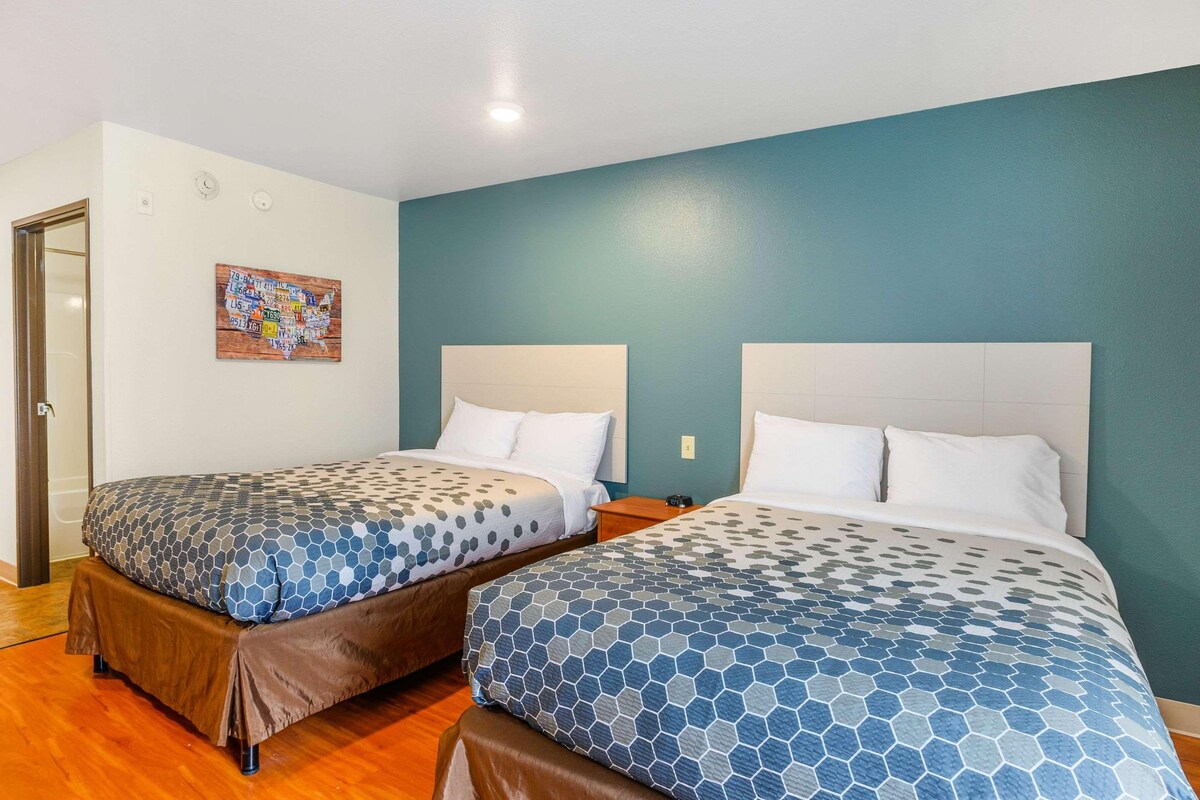 Dos camas individuales con ropa de cama azul y blanca a juego, piso de madera y pared color aguamarina con una obra de arte de un mapa.