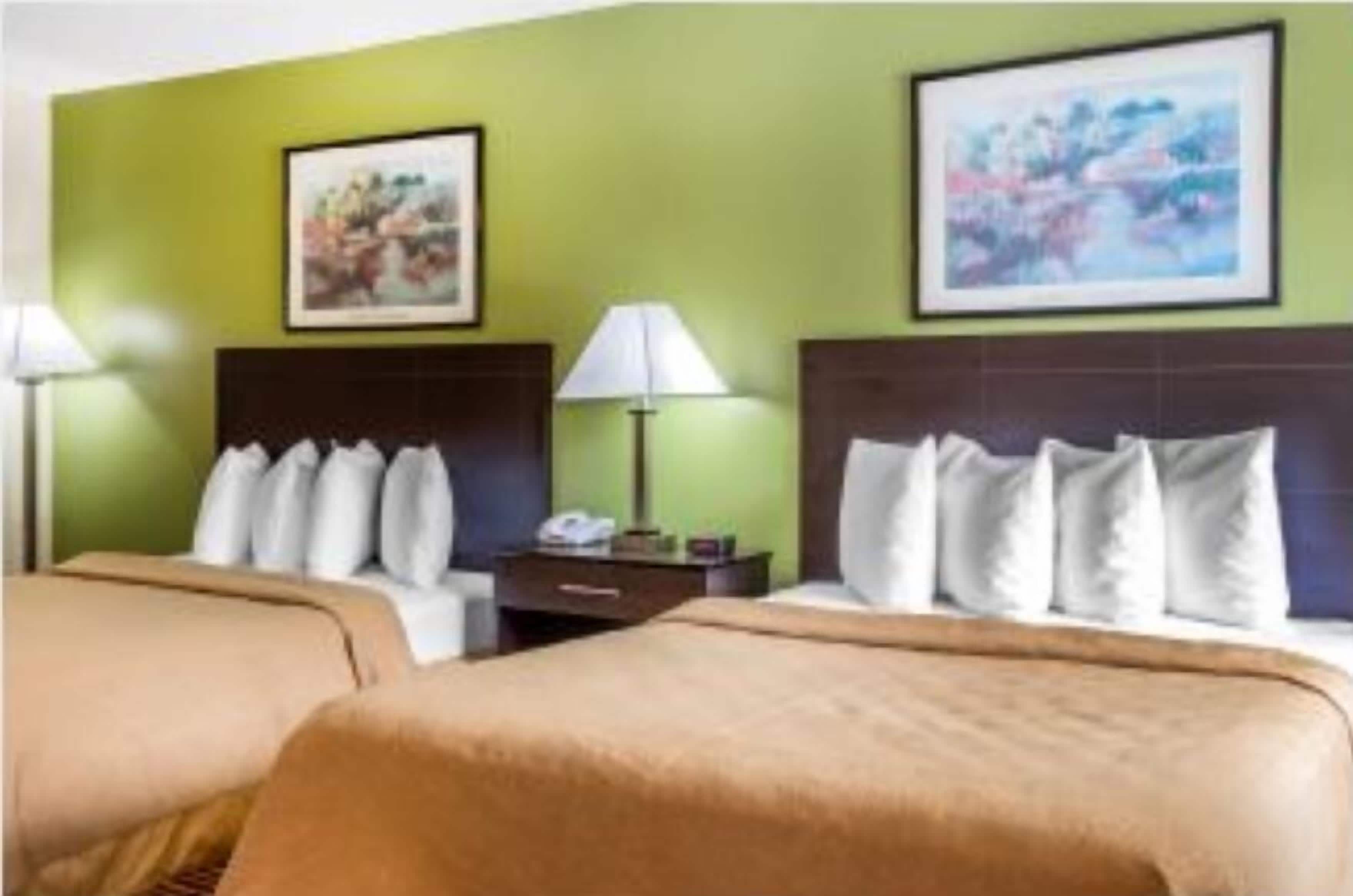 A hotel room with two beds, green walls, and artwork above the beds.