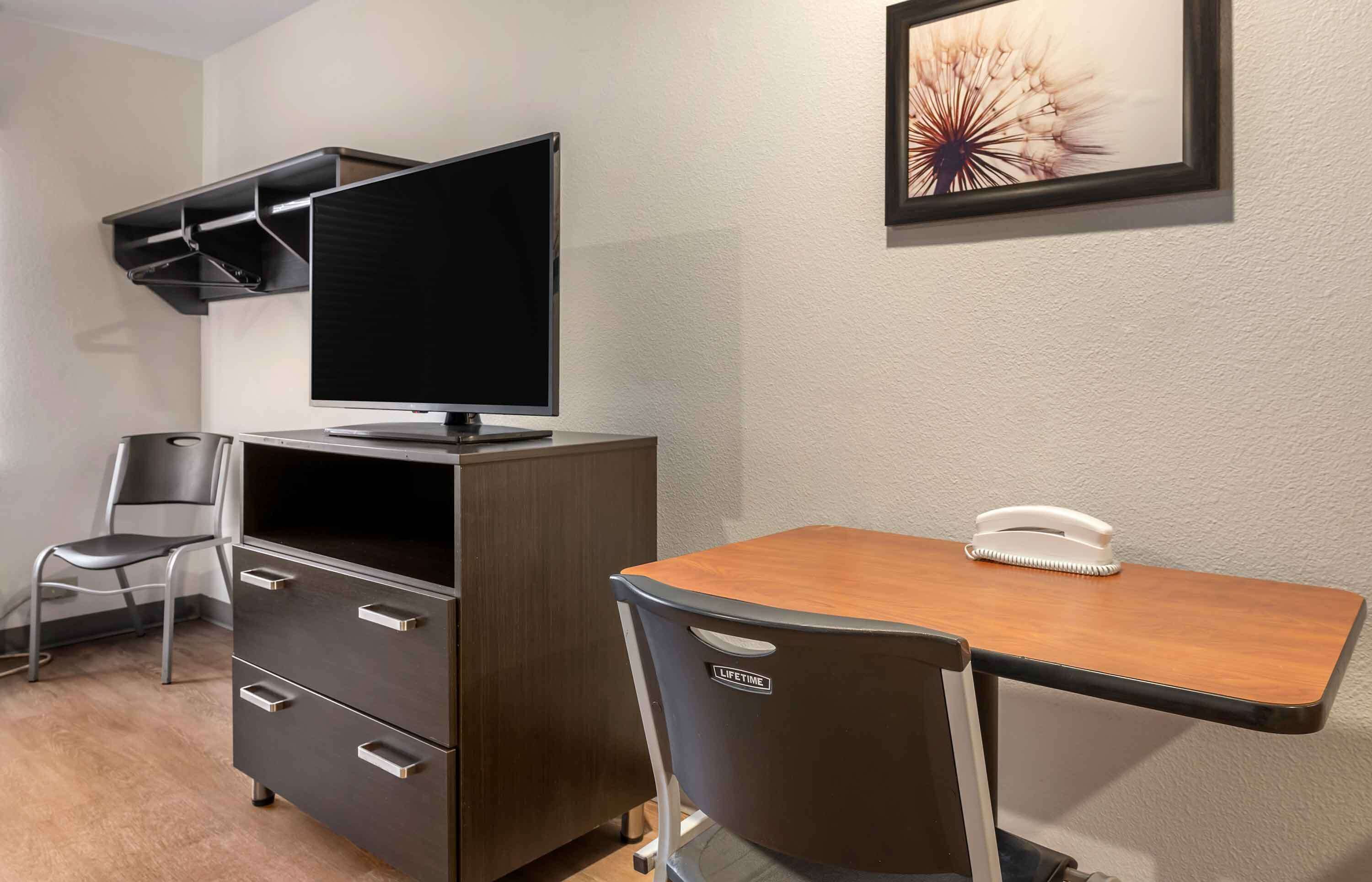 Ein Hotelzimmer mit Schreibtisch, Stuhl, Fernseher und einer kleinen Ablagefläche.