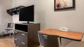 Habitación de hotel con escritorio, silla, televisión y un pequeño estante.