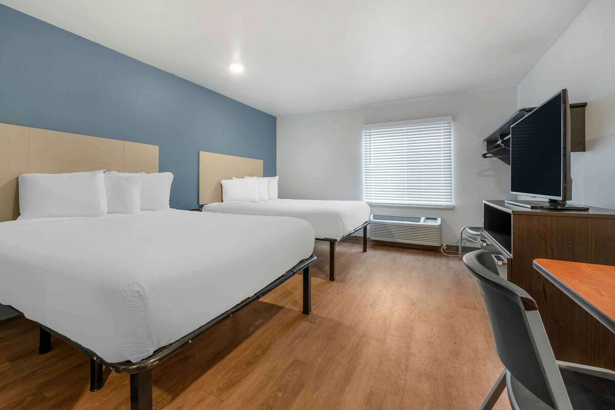 Quarto de hotel com duas camas, uma escrivaninha, televisão e janela com cortinas.