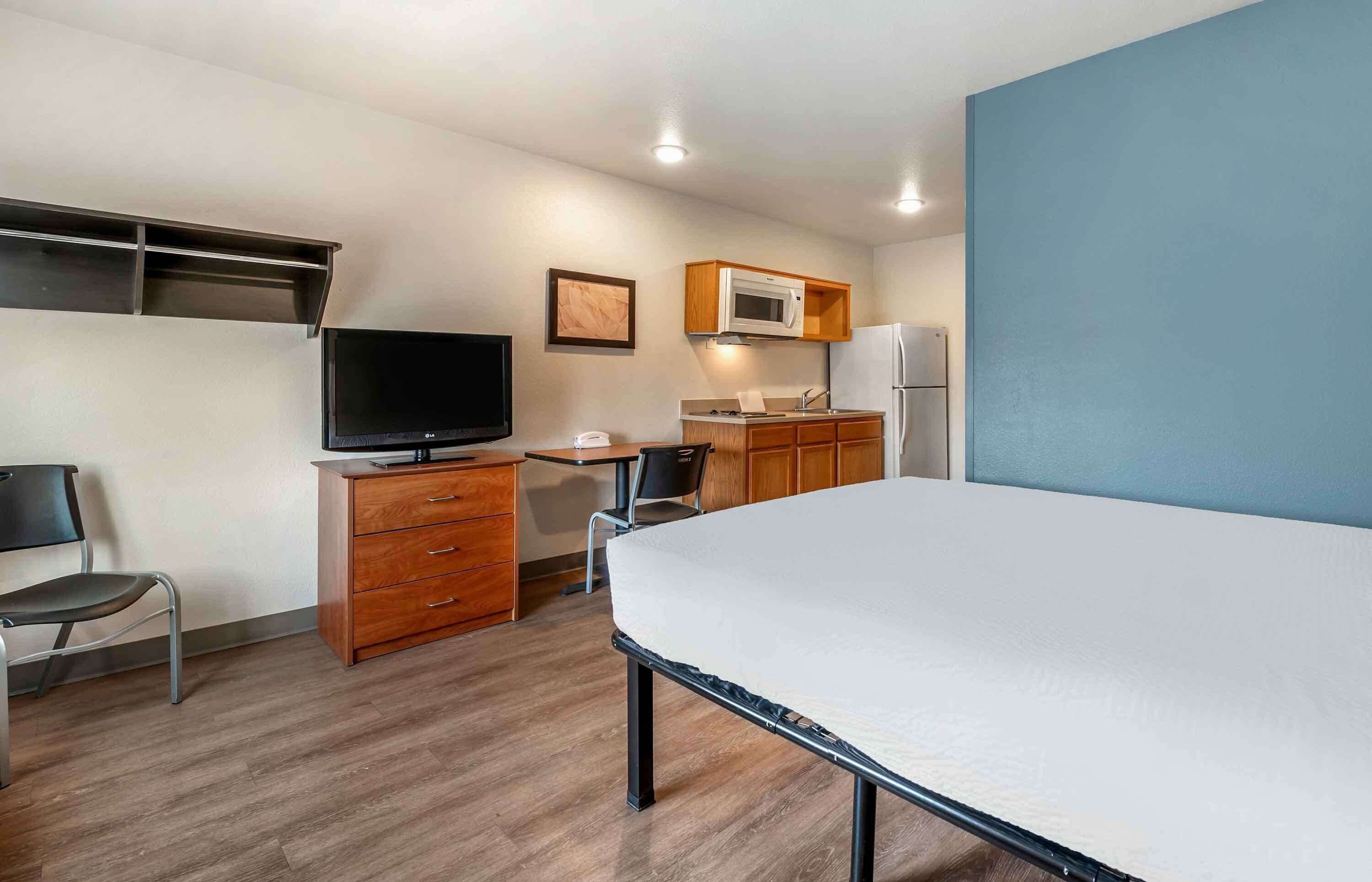 A compact hotel room with a bed, a TV, a desk with a chair, a microwave, and a refrigerator.