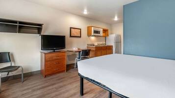 Habitación de hotel compacta con cama, televisor, escritorio con silla, microondas y refrigerador.