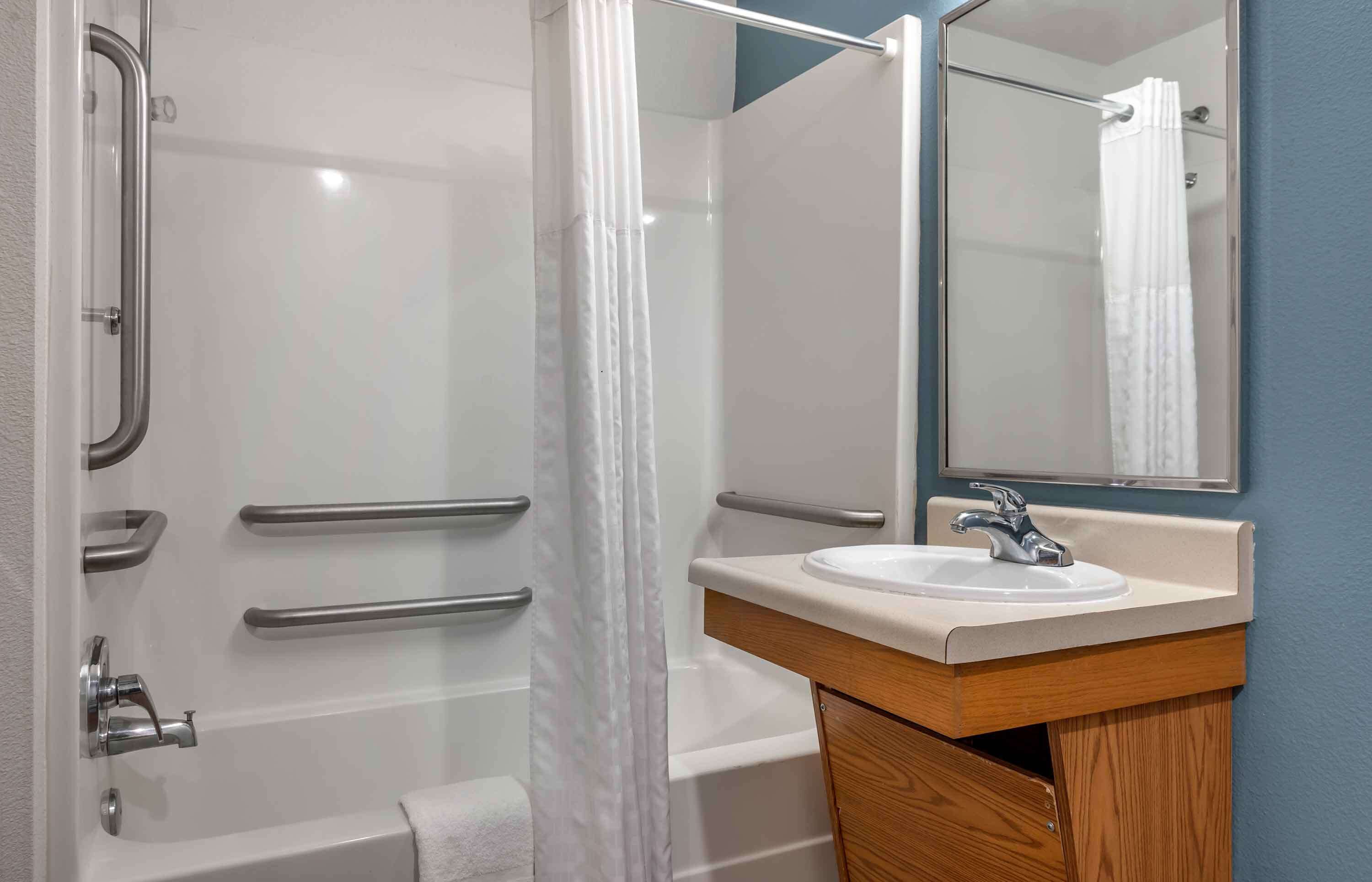 Un baño moderno con cabina de ducha de vidrio, un lavamanos blanco con mueble de madera y un espejo sobre el lavamanos.