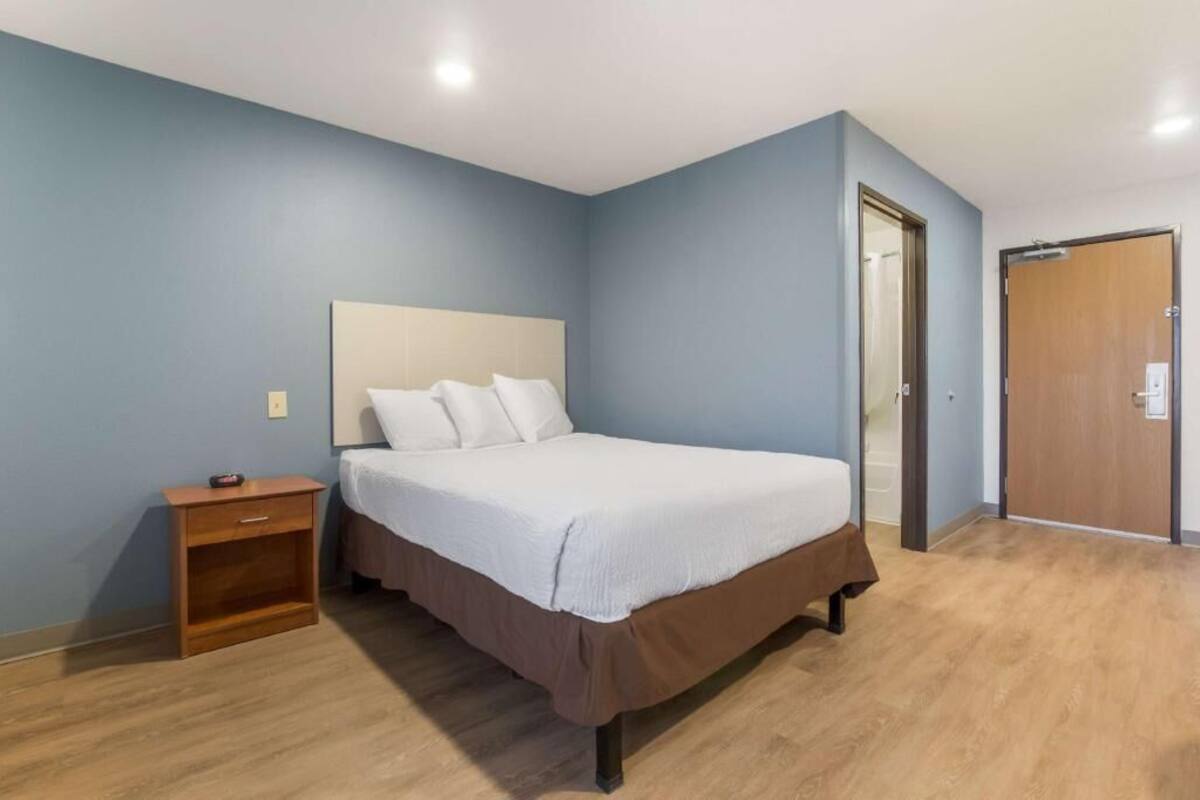 Quarto com cama, mesa de cabeceira e porta de madeira.