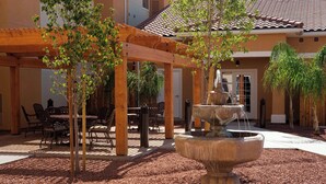 Un patio couvert avec des sièges d’extérieur, une fontaine en pierre et une pergola ornée de plantes grimpantes.
