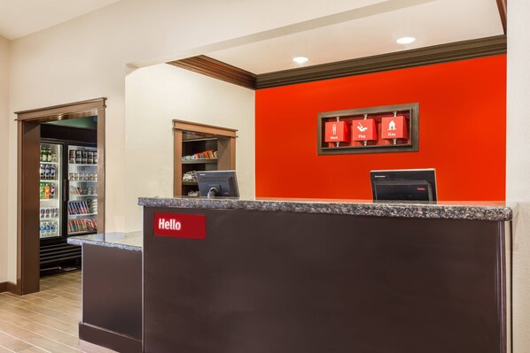 A hotel reception area with a red wall, a 'Hello' sign, a refrigerator, and a small shelf with items.