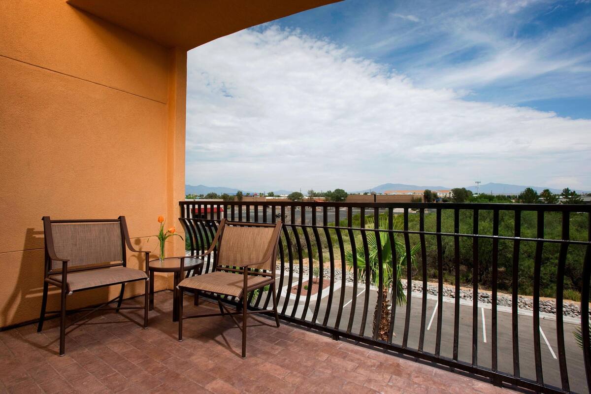 Un balcon avec deux chaises et une petite table, donnant sur un parking et un paysage lointain.