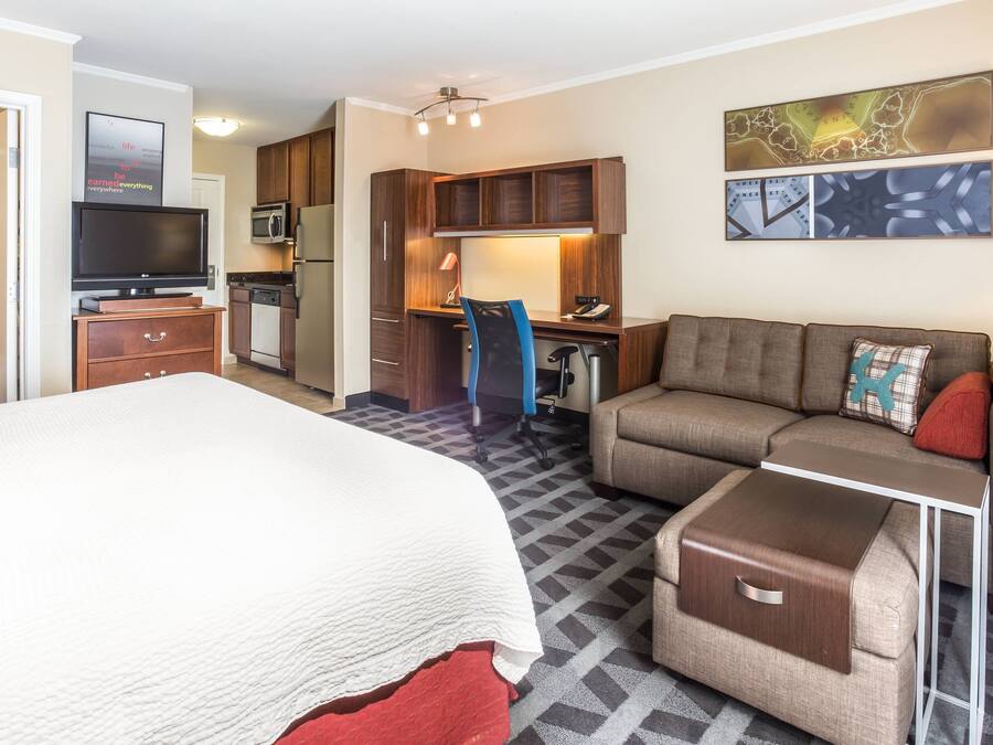 A hotel room with a bed, a sofa, a desk, a chair, a TV, a microwave, and a refrigerator.
