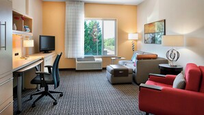 A hotel room with a desk, chair, red sofa, and a window with a view of trees.