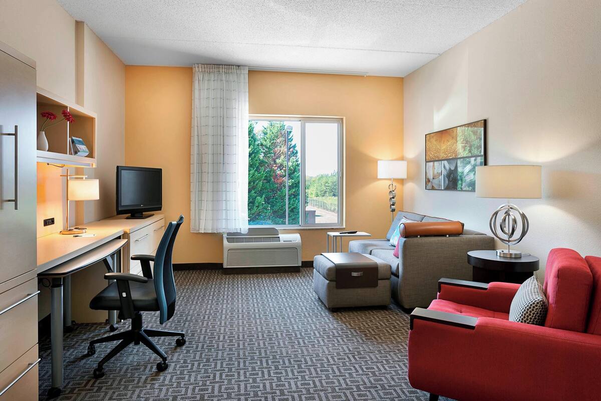 A hotel room with a desk, chair, red sofa, and a window with a view of trees.