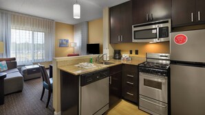 A compact kitchen with a microwave, stove, and dishwasher. There is a dining area with a table and chairs.