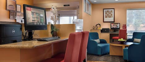 A reception area with a computer, a monitor, a plant, and seating with red and blue chairs.