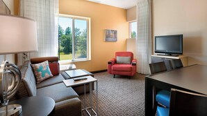 A hotel room with a sofa, armchair, TV, and a small table.