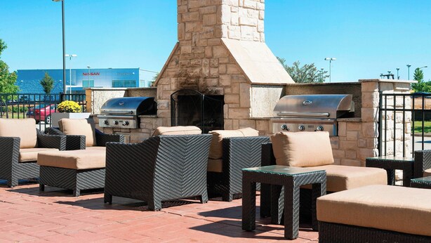 An outdoor patio with wicker furniture and a stone chimney, featuring a grill and a hibachi grill.