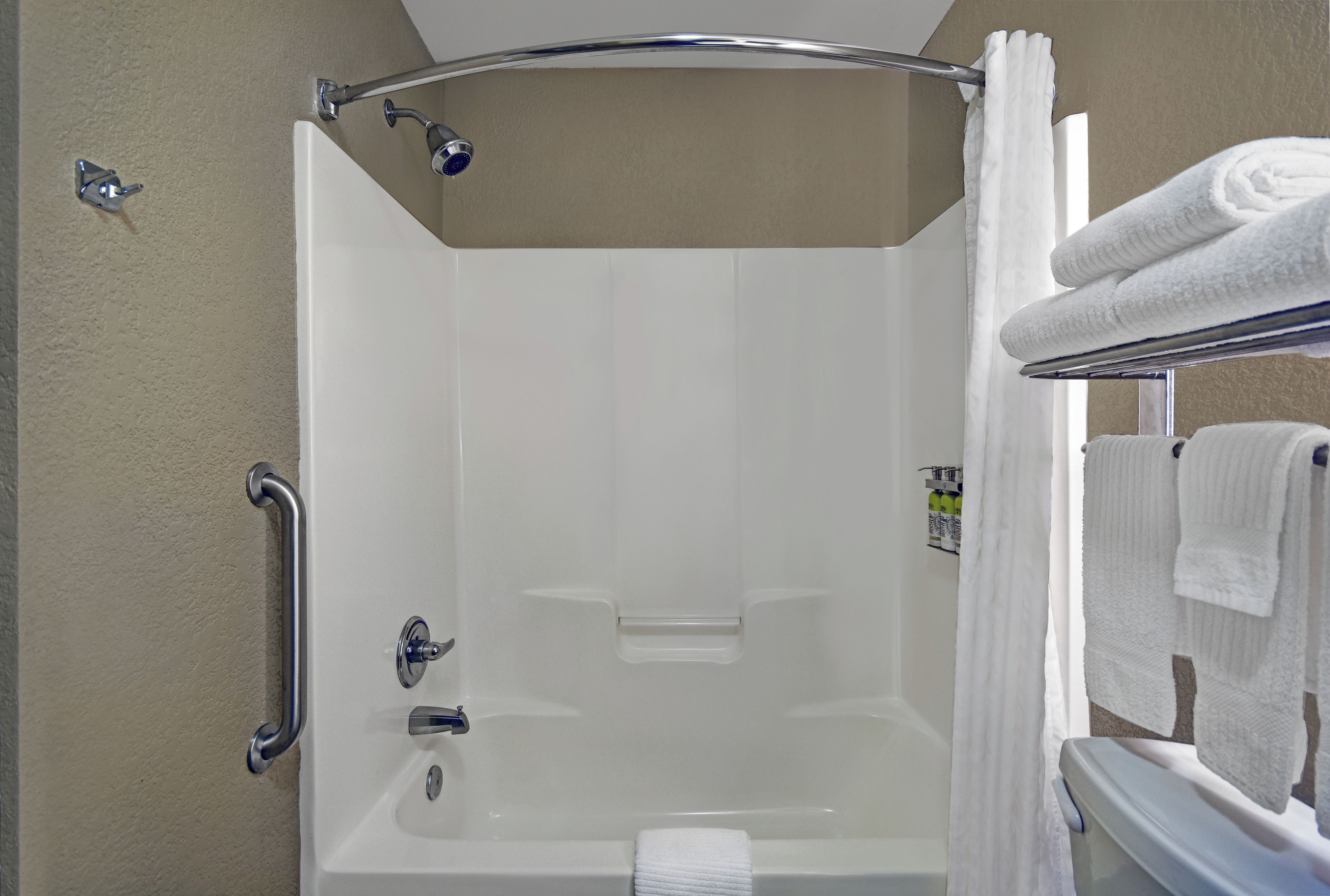 A walk-in shower with a bathtub, a handrail, and a towel rack with towels.
