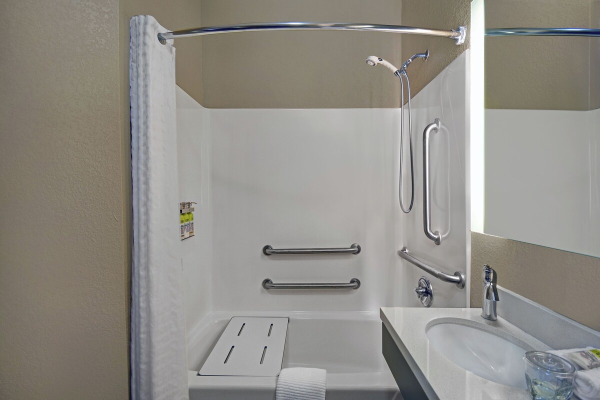 A bathroom with a shower, grab bars, a towel rack, and a sink.