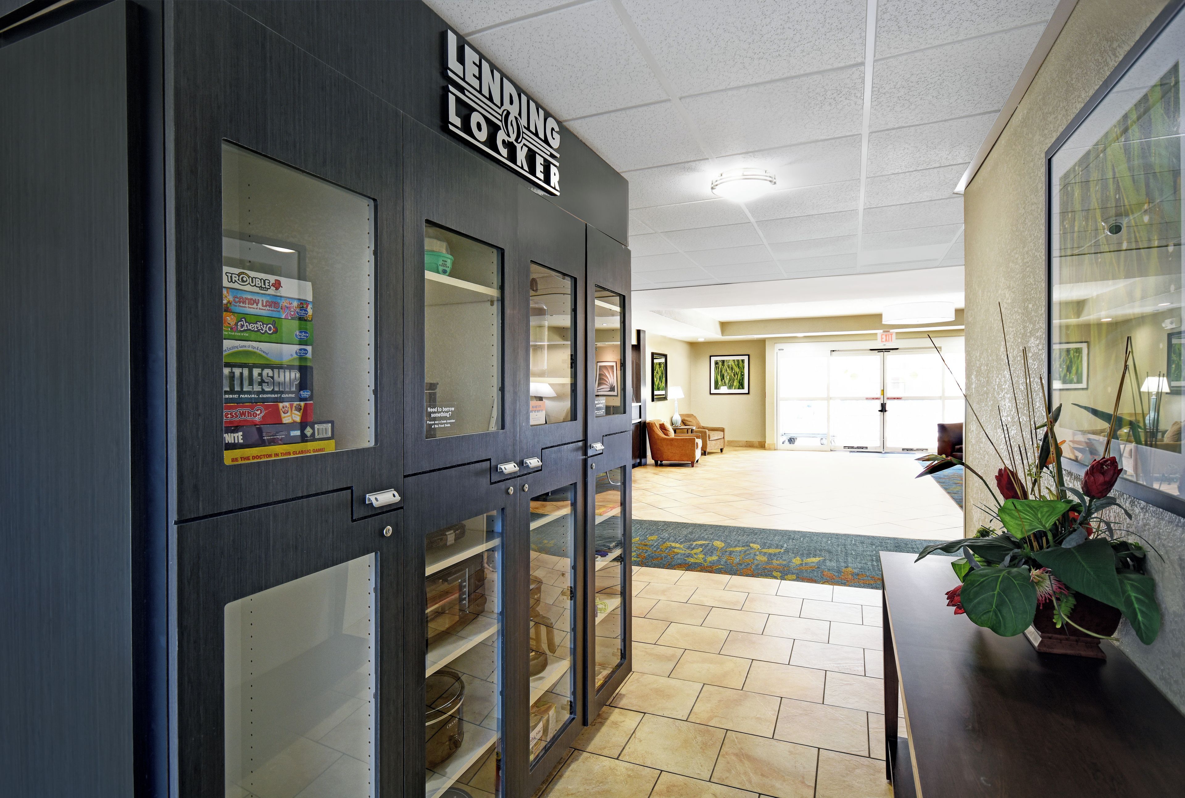 A hotel lobby with a lending locker, a reception area, and a seating area with a view of the outdoors.