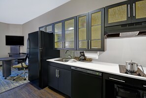 A modern kitchen with dark cabinets, a built-in dishwasher, a coffee maker, and a flat-screen TV. - Candlewood Suites Sumter by IHG (Sumter)
