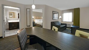 A hotel room with a dining area, a bed, a bathroom, and a large window with curtains. - Candlewood Suites Sumter by IHG (Sumter)