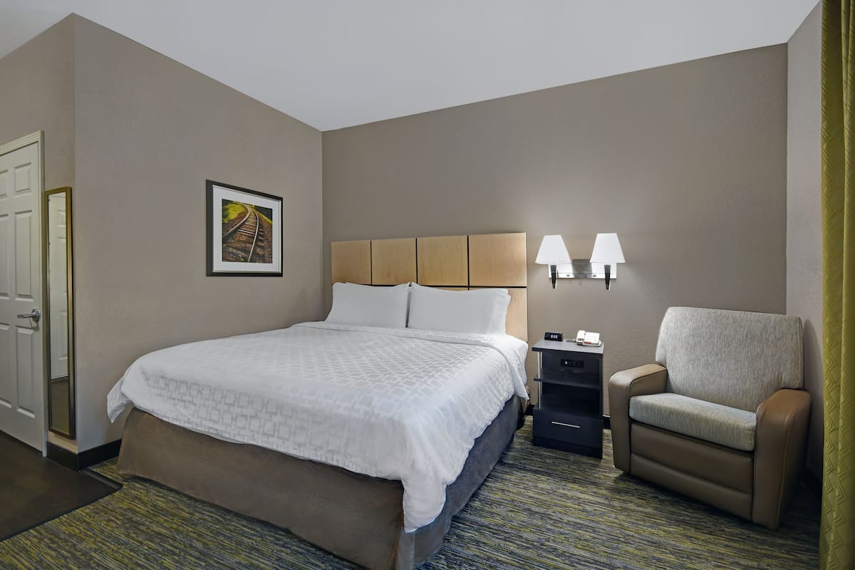 Una habitación de hotel con cama, una silla, una mesita de noche y una lámpara de pared.