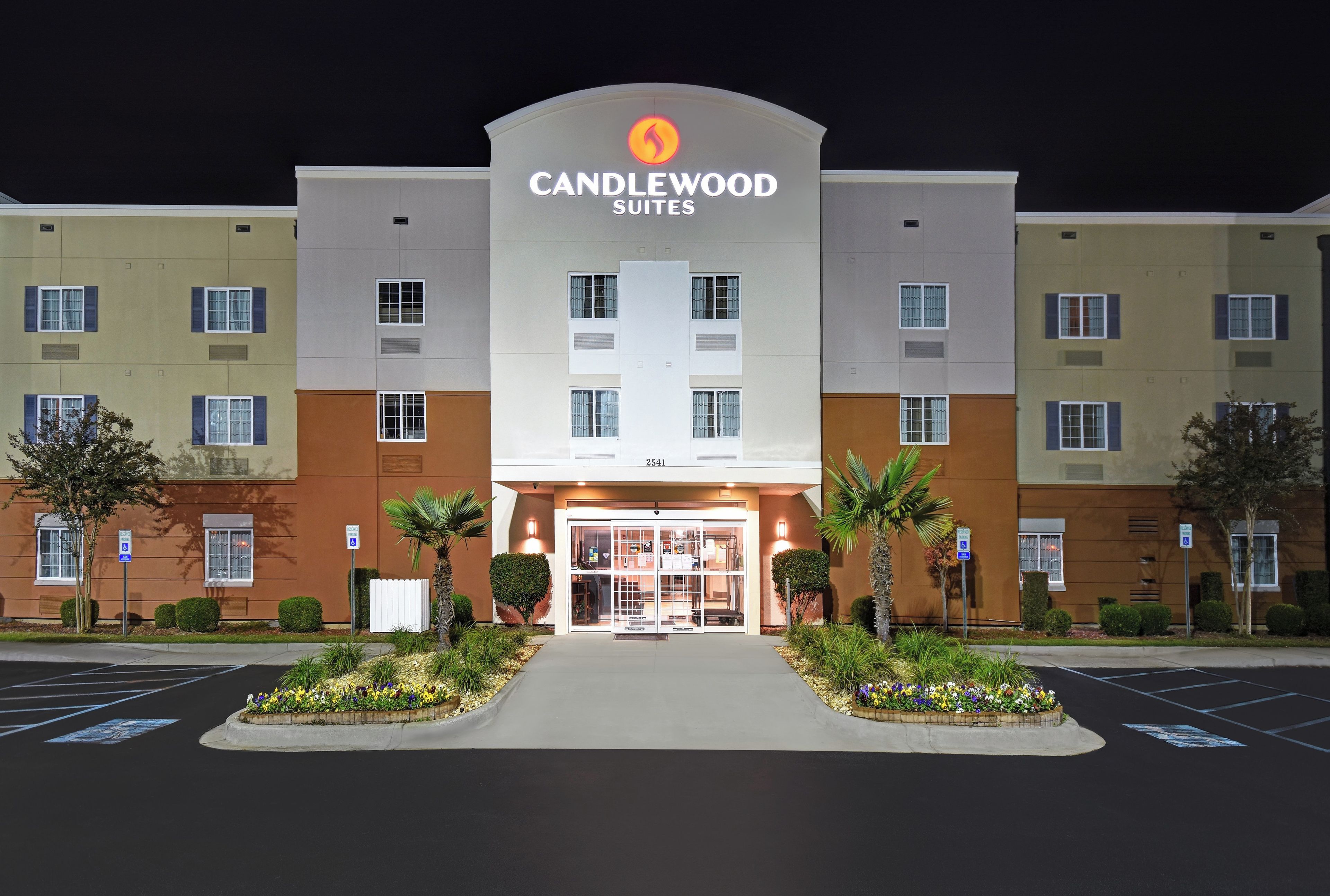 A hotel entrance with a sign reading 'CANDLEWOOD SUITES' and a parking lot in front.