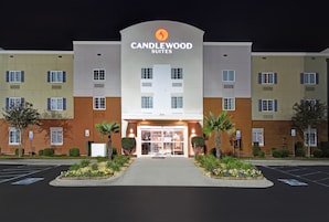 Entrada de un hotel con un cartel que dice 'CANDLEWOOD SUITES' y un estacionamiento al frente.