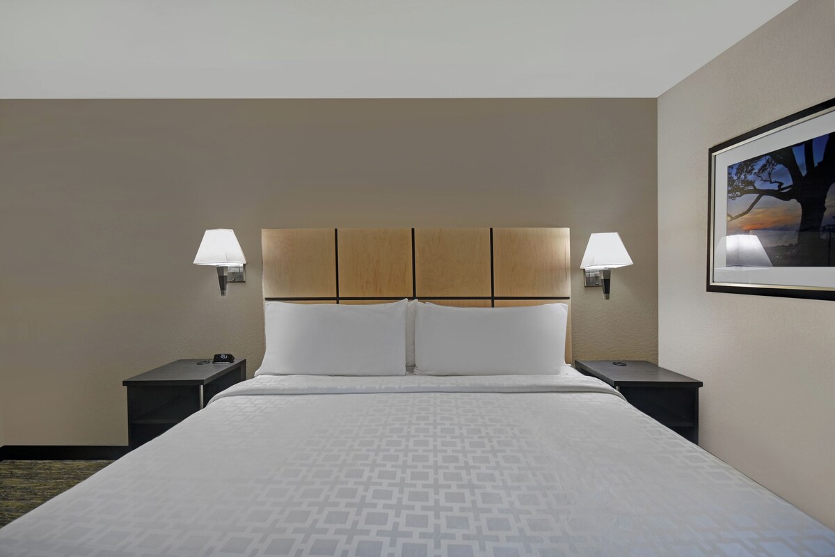 A hotel room with a large bed, two bedside tables, and a headboard with integrated lighting.