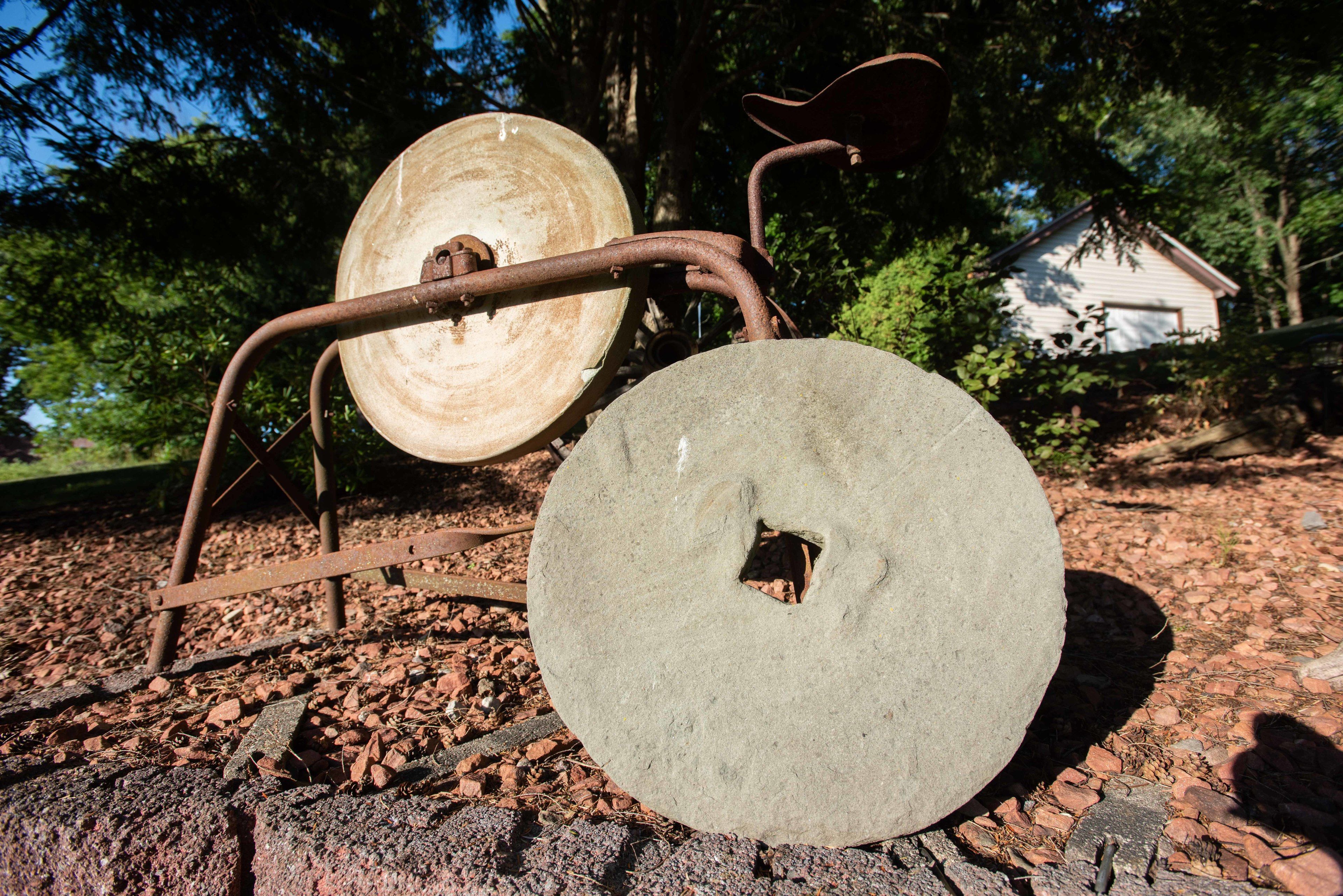 Een landelijke buitenomgeving met een groot wiel en metalen constructie, mogelijk onderdeel van een historische of landbouwexpositie.