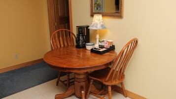 Una mesa de madera para comer con cuatro sillas, una cafetera, una lámpara y una bandeja con salsas y aderezos.