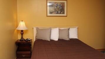 A bedroom with a bed, pillows, a nightstand, a lamp, and a framed picture on the wall.