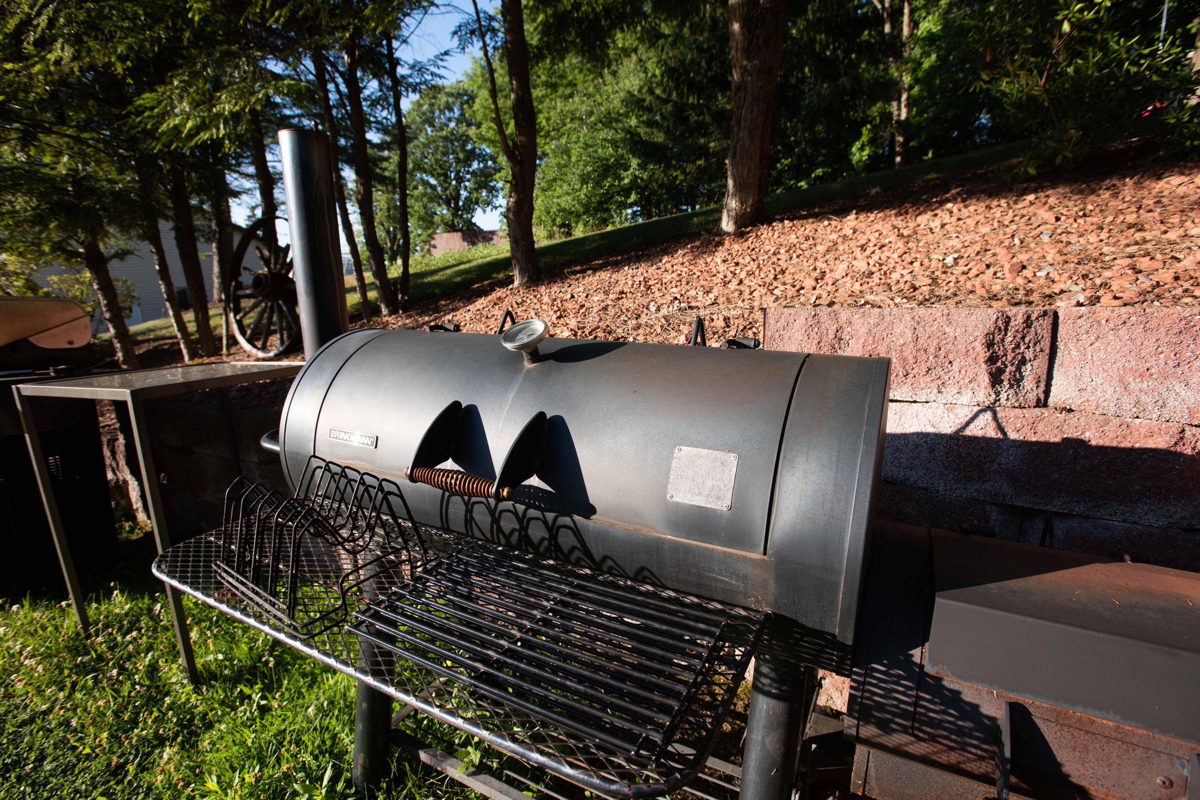 Una parrilla portátil con rejilla de metal, instalada al aire libre con árboles de fondo.