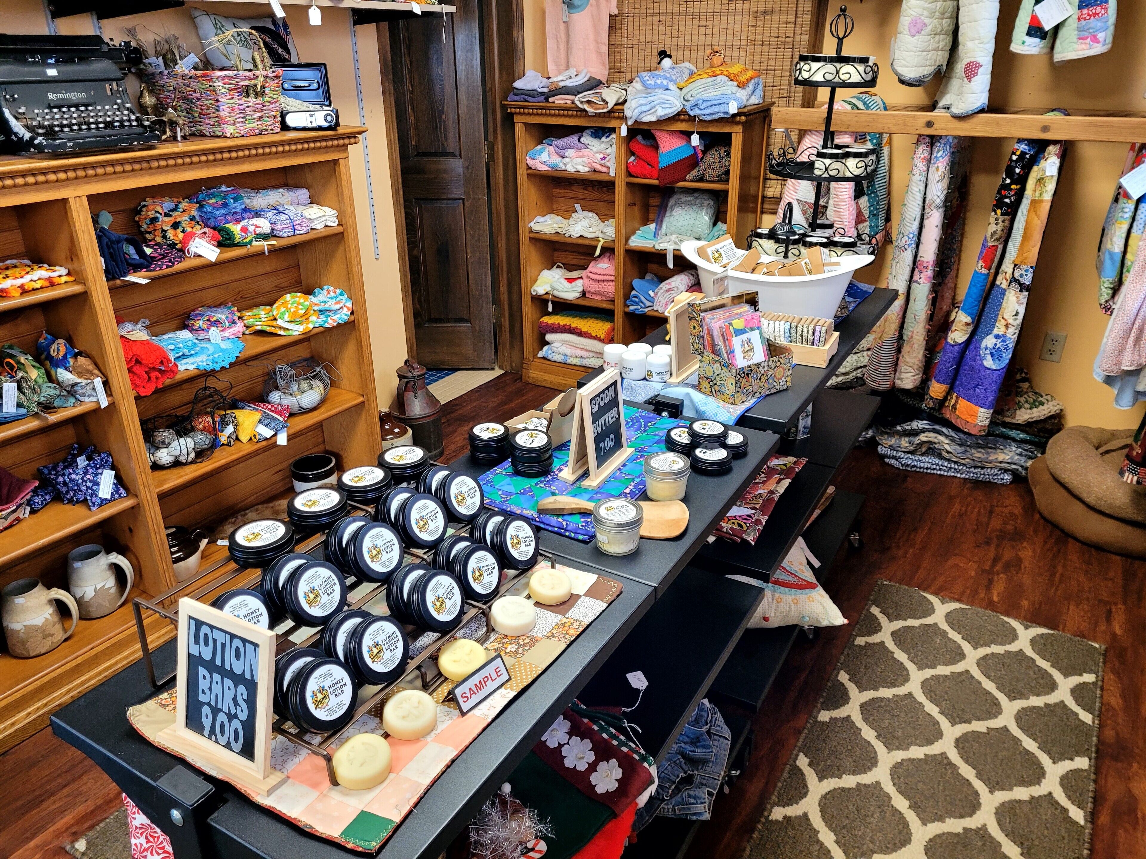 A store with shelves of colorful fabrics, a display of jars labeled 'Honey & Oat Bar', and a sign for 'Spoon Butter' priced at 1.00.
