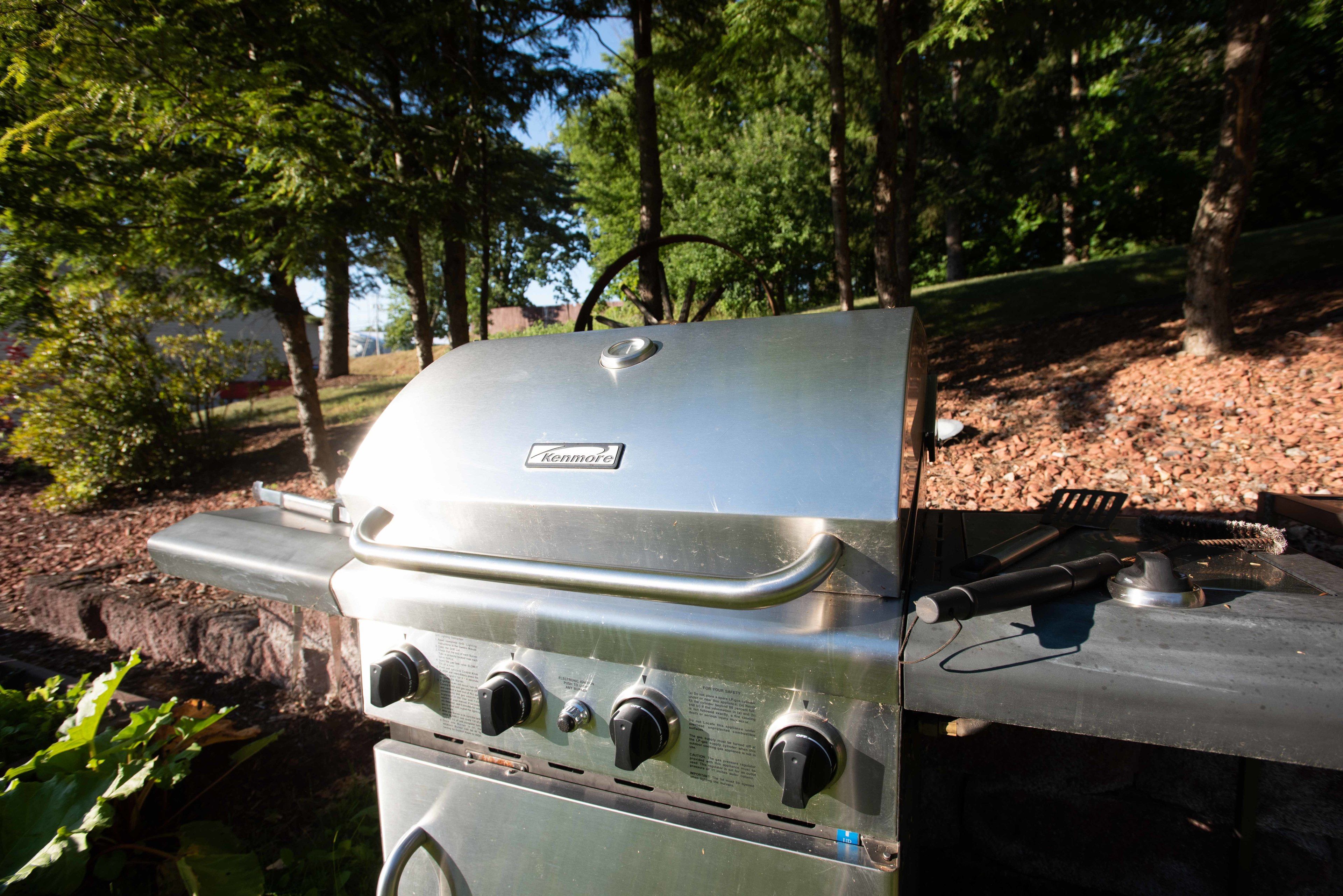 A Kenmore grill with four burners, located outdoors with trees in the background.