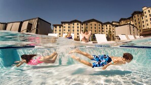A swimming pool with clear water, lounge chairs, and a building in the background. - Great Wolf Lodge Concord (Concord)