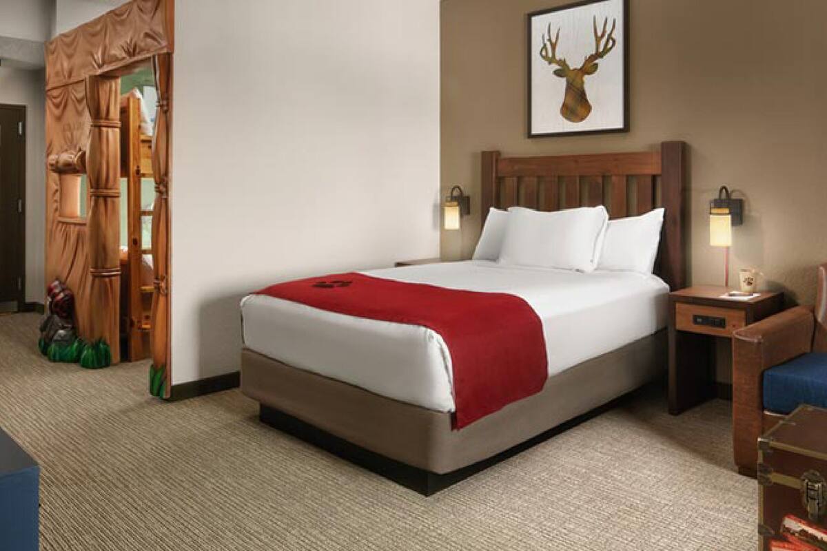 A hotel room with a bed, a nightstand, a chair, and a painting of a deer head on the wall.