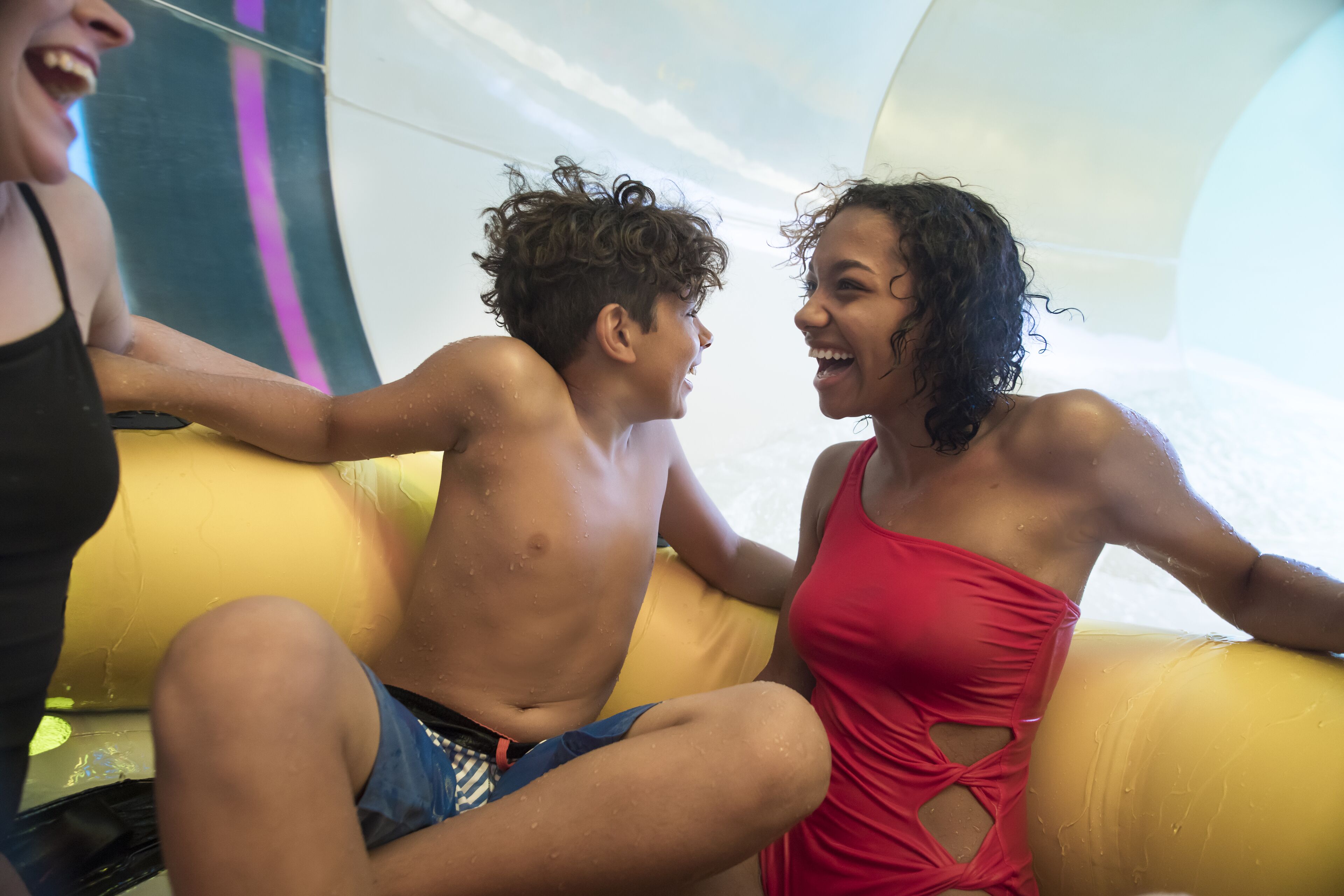 A person sitting on a yellow inflatable tube in a room with a curved ceiling and a visible water slide.