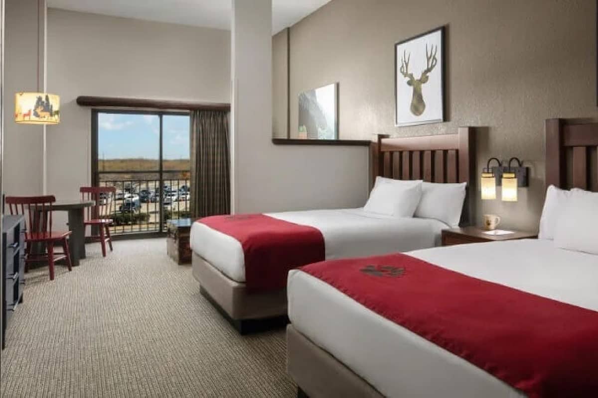 A hotel room with two beds, a balcony with a view, and a dining area with chairs.