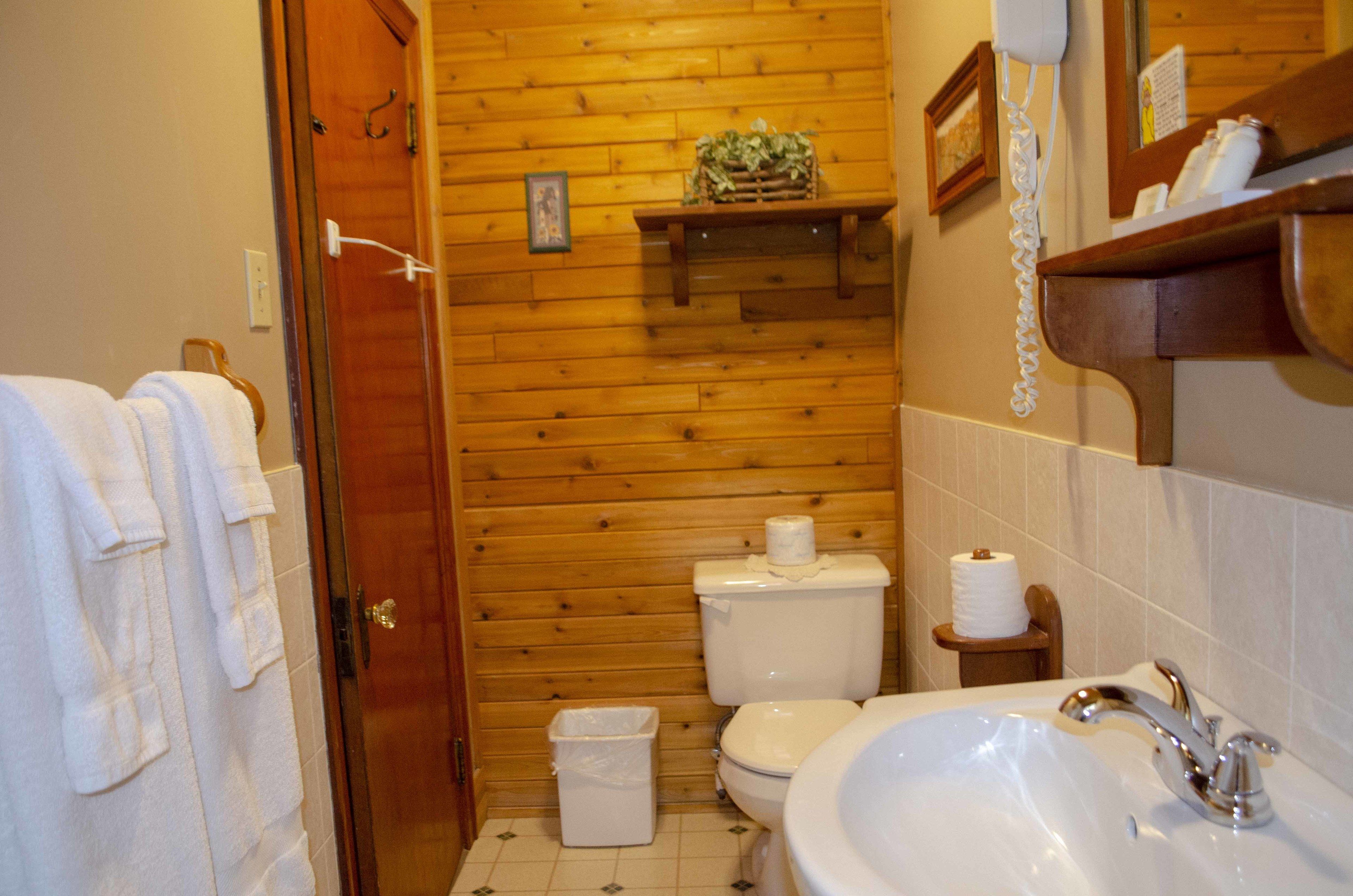 A wooden-paneled bathroom with a toilet, sink, and a small shelf with toiletries.