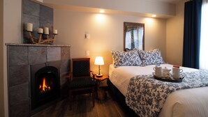Hotelkamer met een open haard, een bed met bloemenbedrukte lakens, een nachtkastje met een lamp en een dienblad met kopjes en een theepot.
