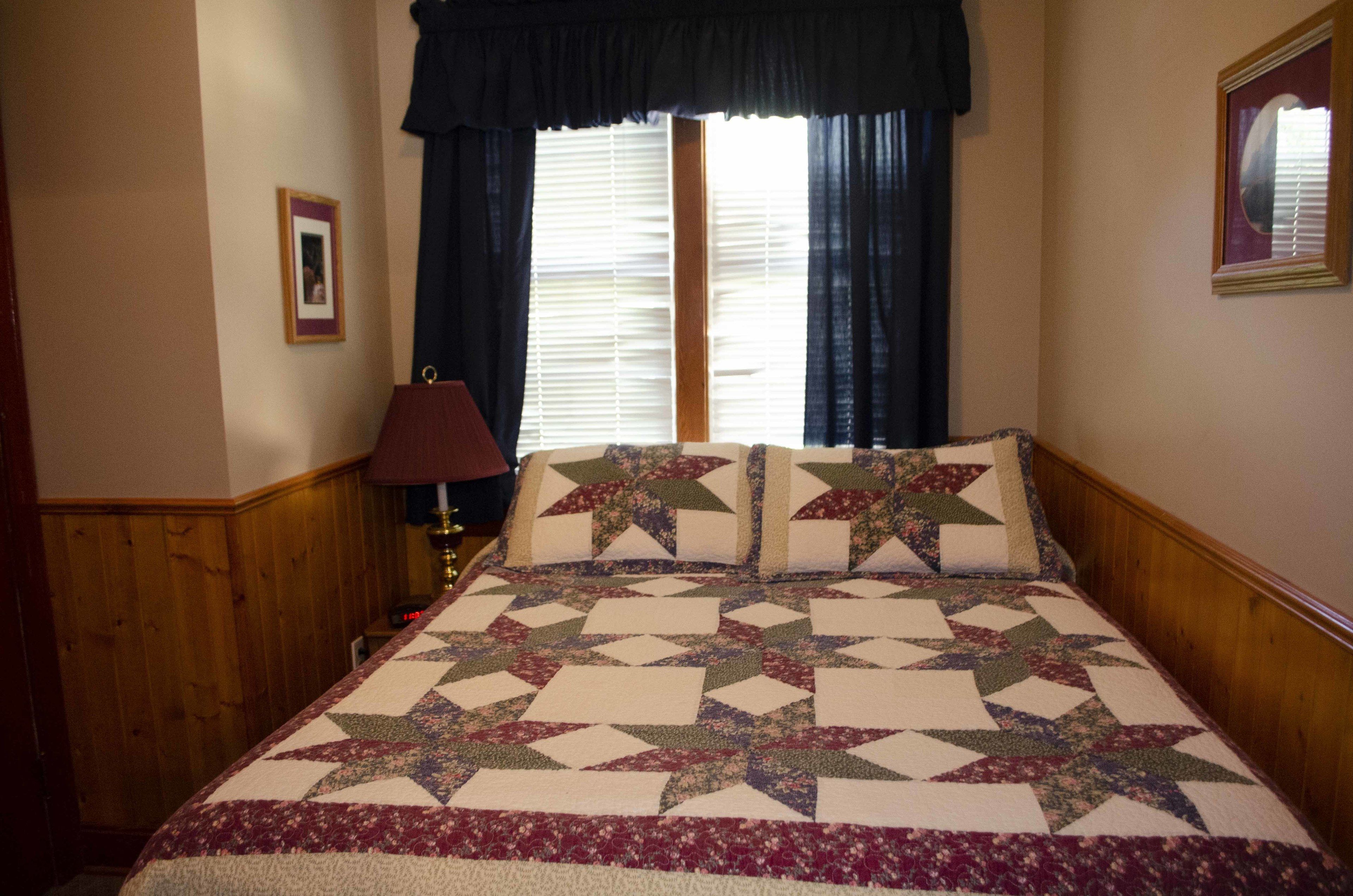 Een slaapkamer met een groot bed, een nachtkastje, een lamp en een raam met gordijnen.